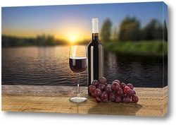    Бутылка красного вина, виноград и бокал на фоне заката
